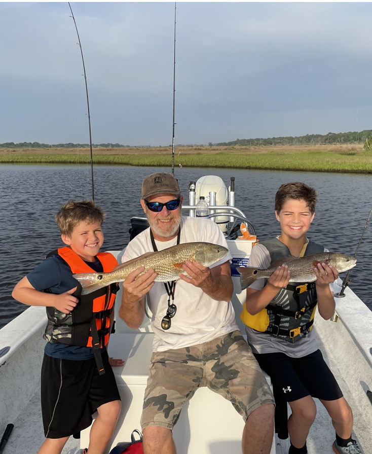 Two young anglers with Captain Mike Hoffman holding a fish on his boat on Topsail Island.